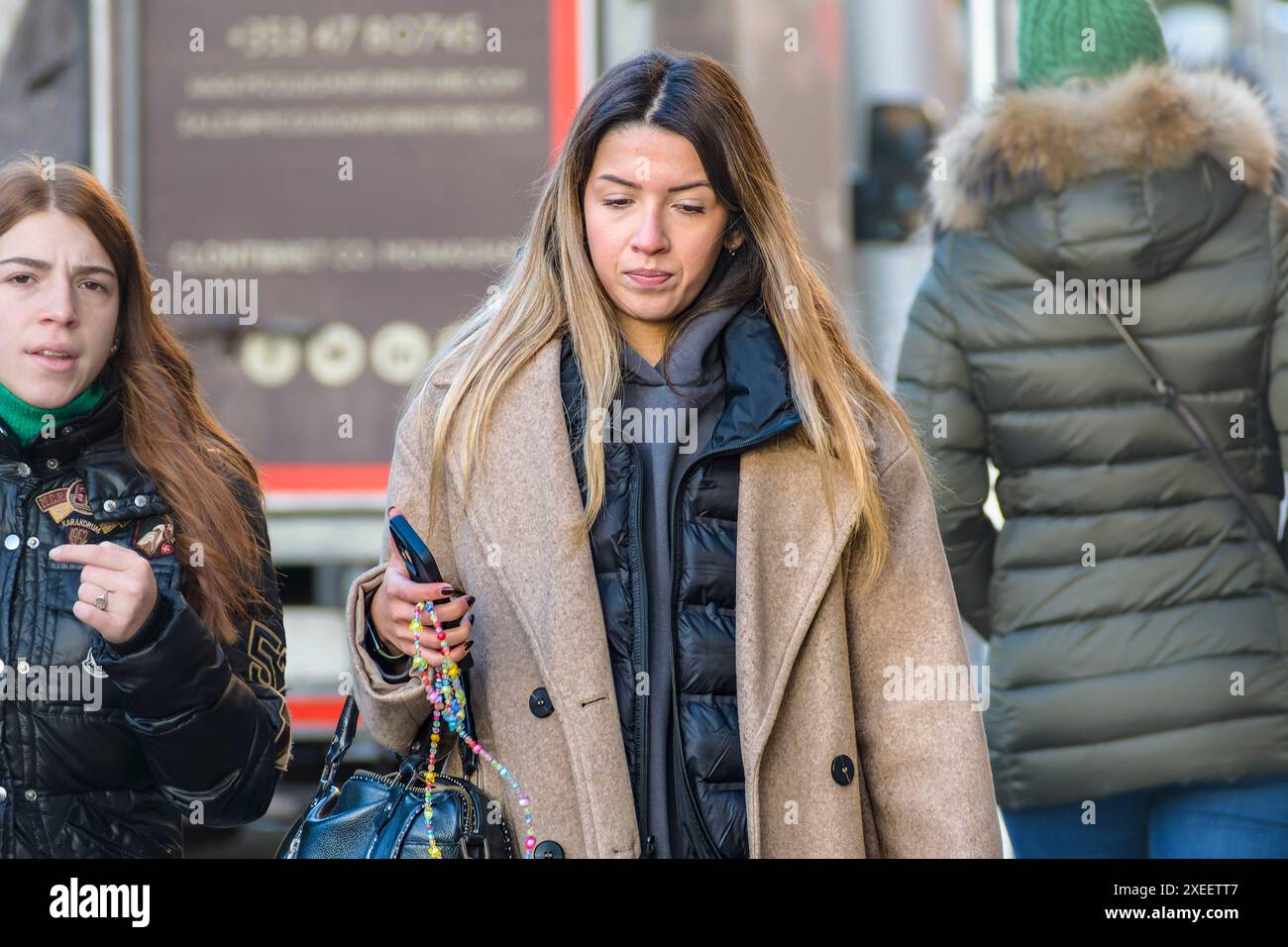 La vita di tutti i giorni. Giovane donna in città con il suo cellulare mentre cammina per una strada cittadina. Dublino, Irlanda. Foto Stock