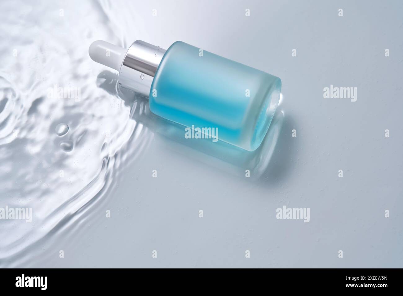 Bottiglie di cosmetici con contagocce in acqua su sfondo blu. Foto Stock