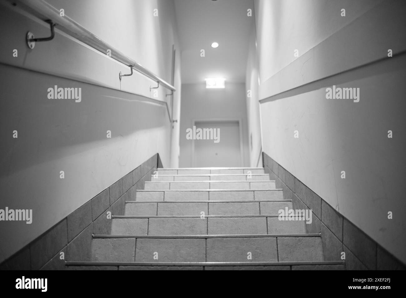 Gradini che precedono e un semaforo alla fine del corridoio con un cartello luminoso di uscita. Un corridoio con gradini, illuminati da lampade, ringhiere, porta all'en Foto Stock