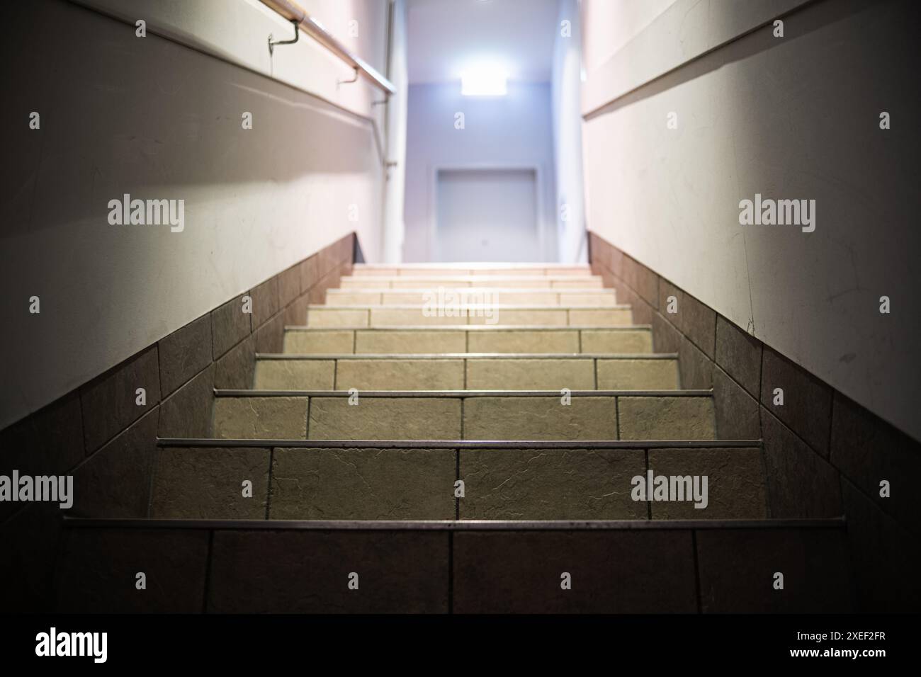 Gradini che precedono e un semaforo alla fine del corridoio con un cartello luminoso di uscita. Un corridoio con gradini, illuminati da lampade, ringhiere, porta all'en Foto Stock