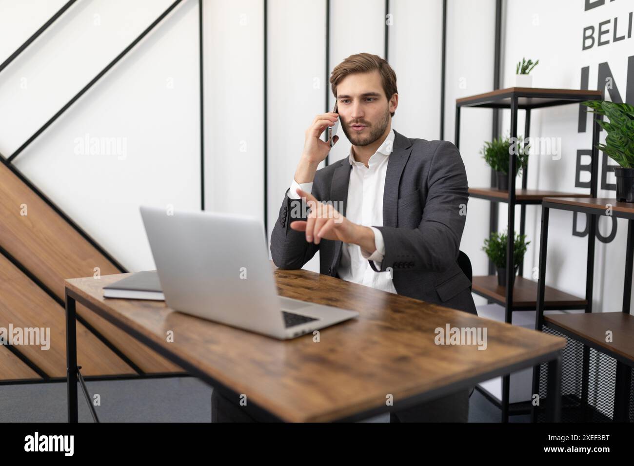 Un avvocato impegnato che parla al telefono in ufficio con un cliente e guarda un portatile Foto Stock