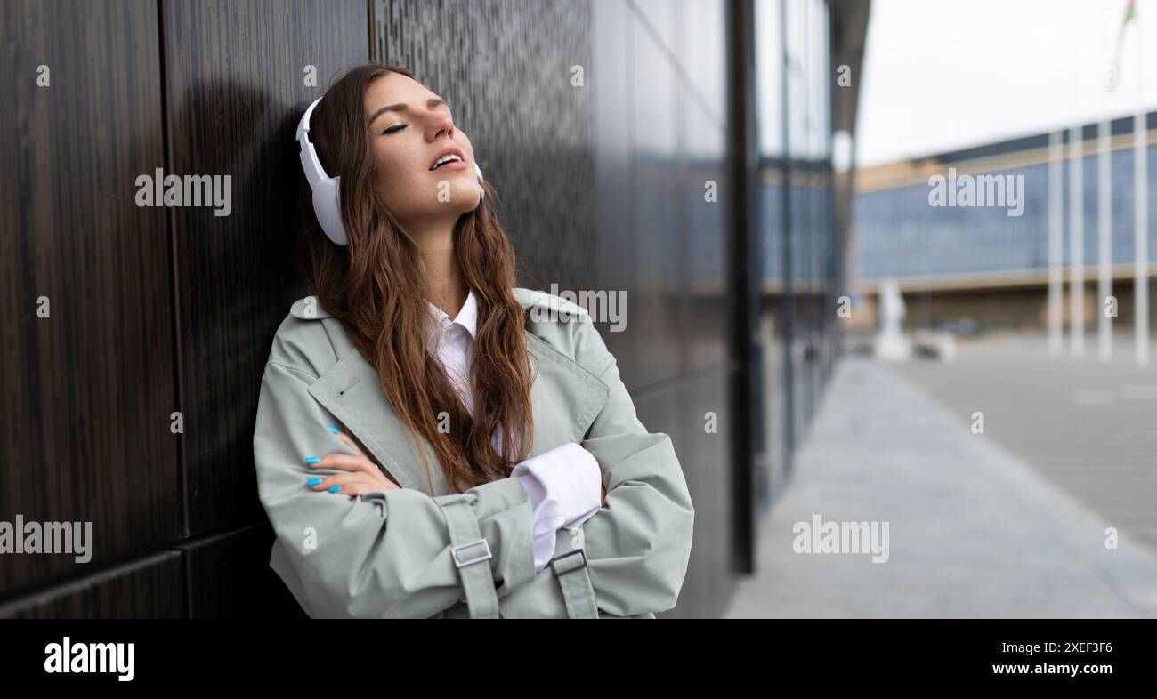 Libera dal lavoro giovane donna che cammina per la strada indossando cuffie wireless di grandi dimensioni Foto Stock