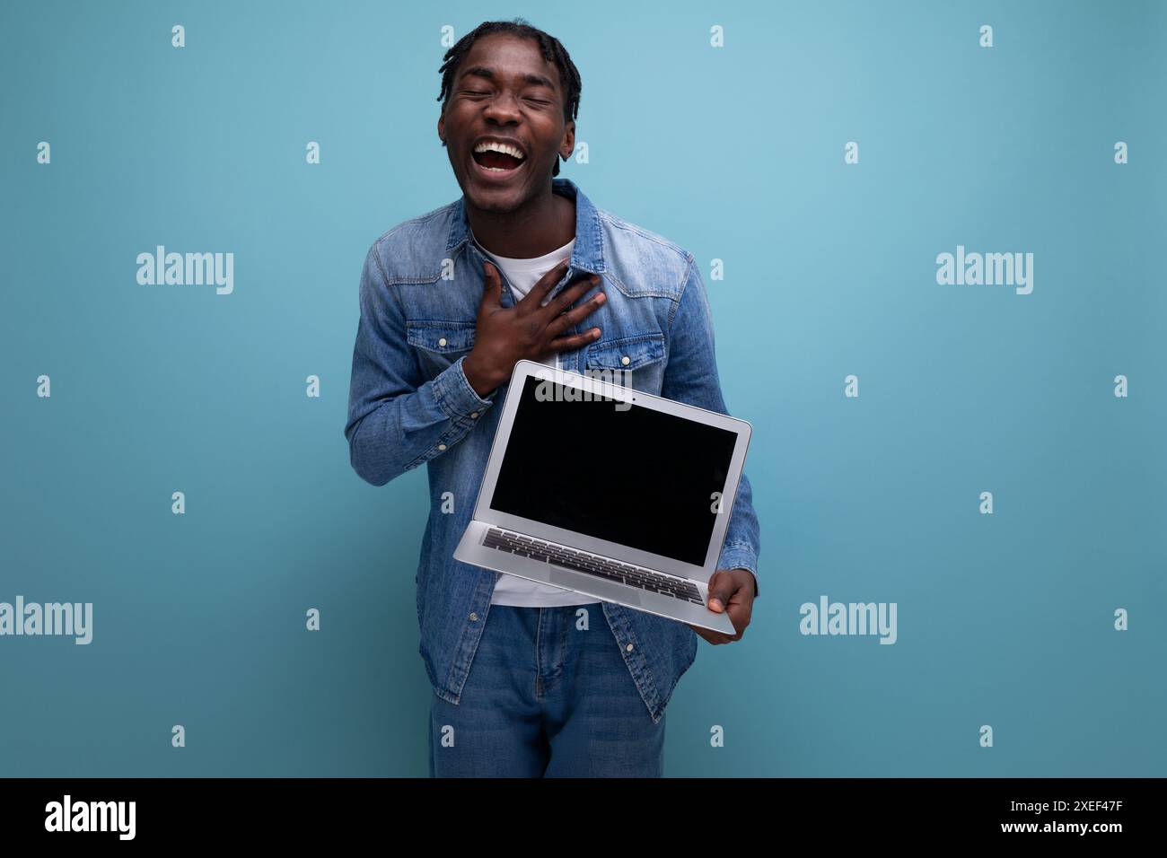 Un freelance di successo americano con dreadlock in giacca di denim lavora in remoto utilizzando un computer portatile Foto Stock