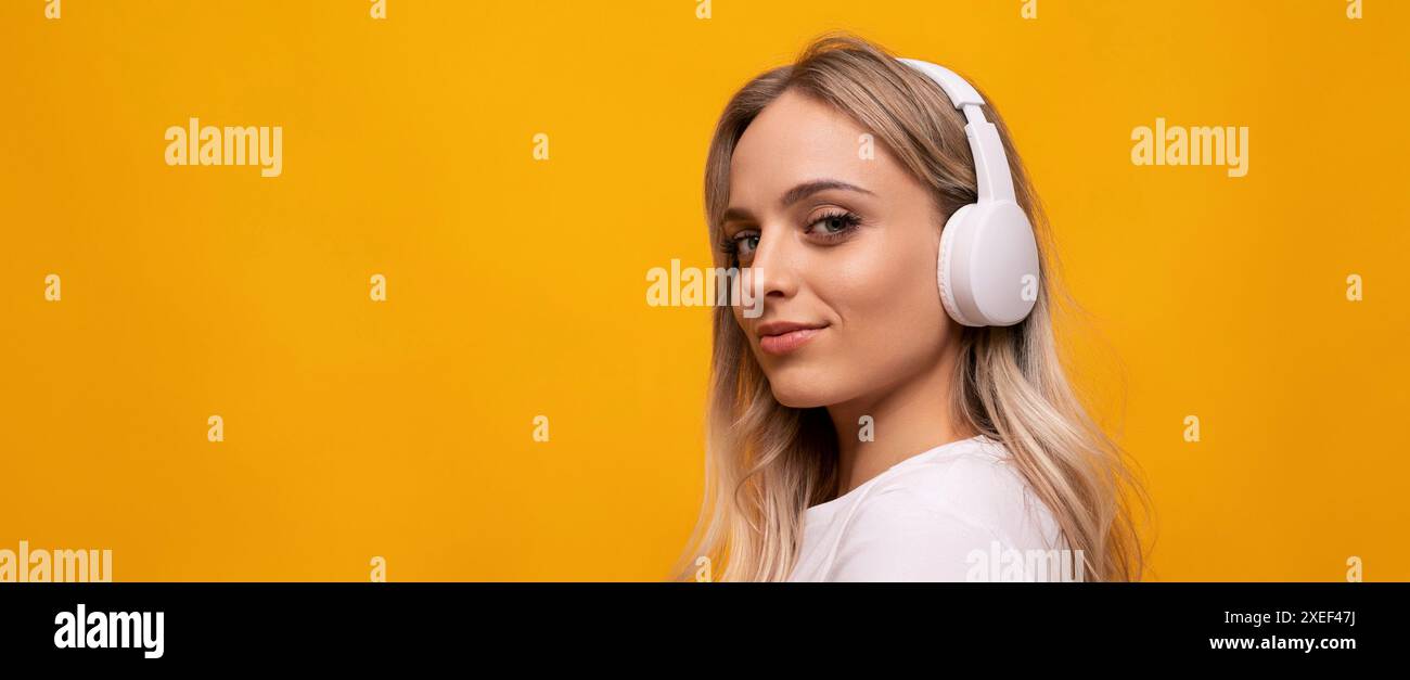 Donna bionda caucasica in posa con cuffie bianche su sfondo arancione con spazio vuoto Foto Stock