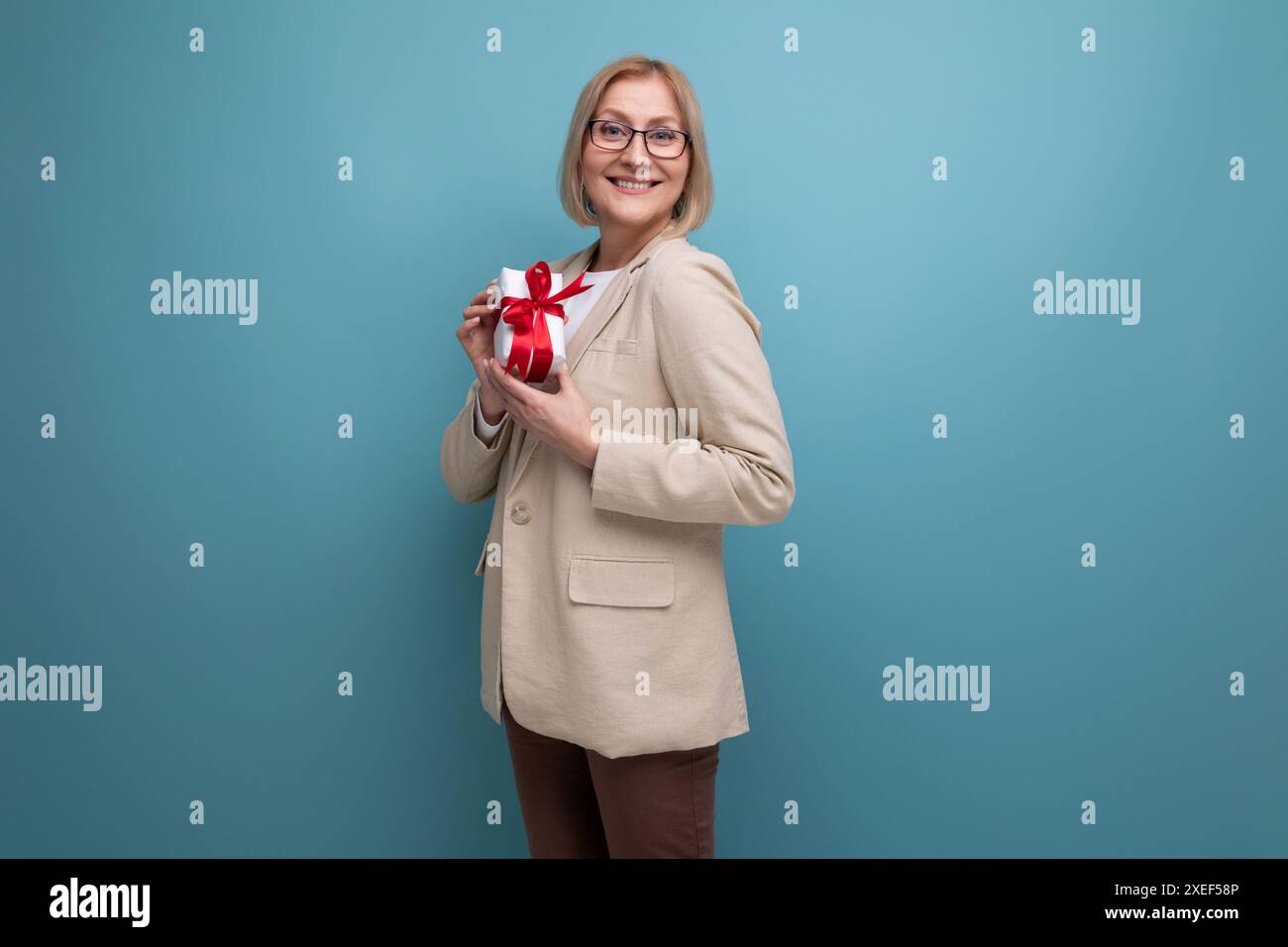 Gioiosa donna matura anni '50 in giacca con confezione regalo su sfondo studio con spazio per copie Foto Stock