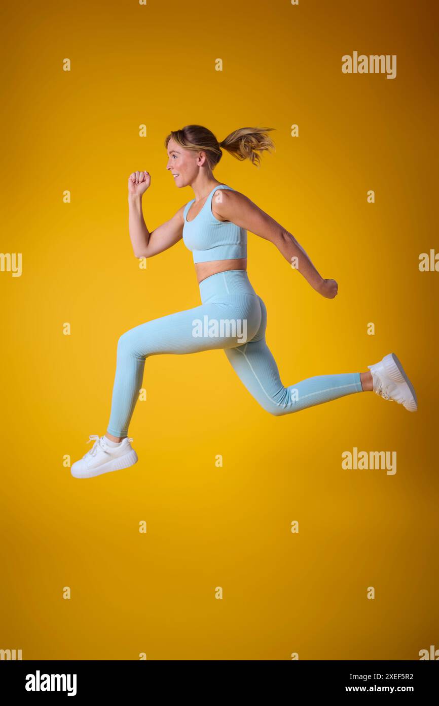 Foto in studio di una donna che indossa un abbigliamento fitness da palestra a mezz'aria su sfondo giallo Foto Stock