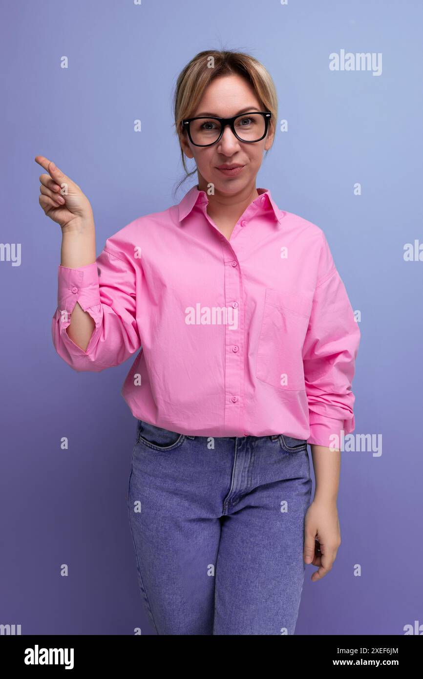 Giovane donna bionda caucasica con occhiali e coda di cavallo vestita con una blusa rosa Foto Stock