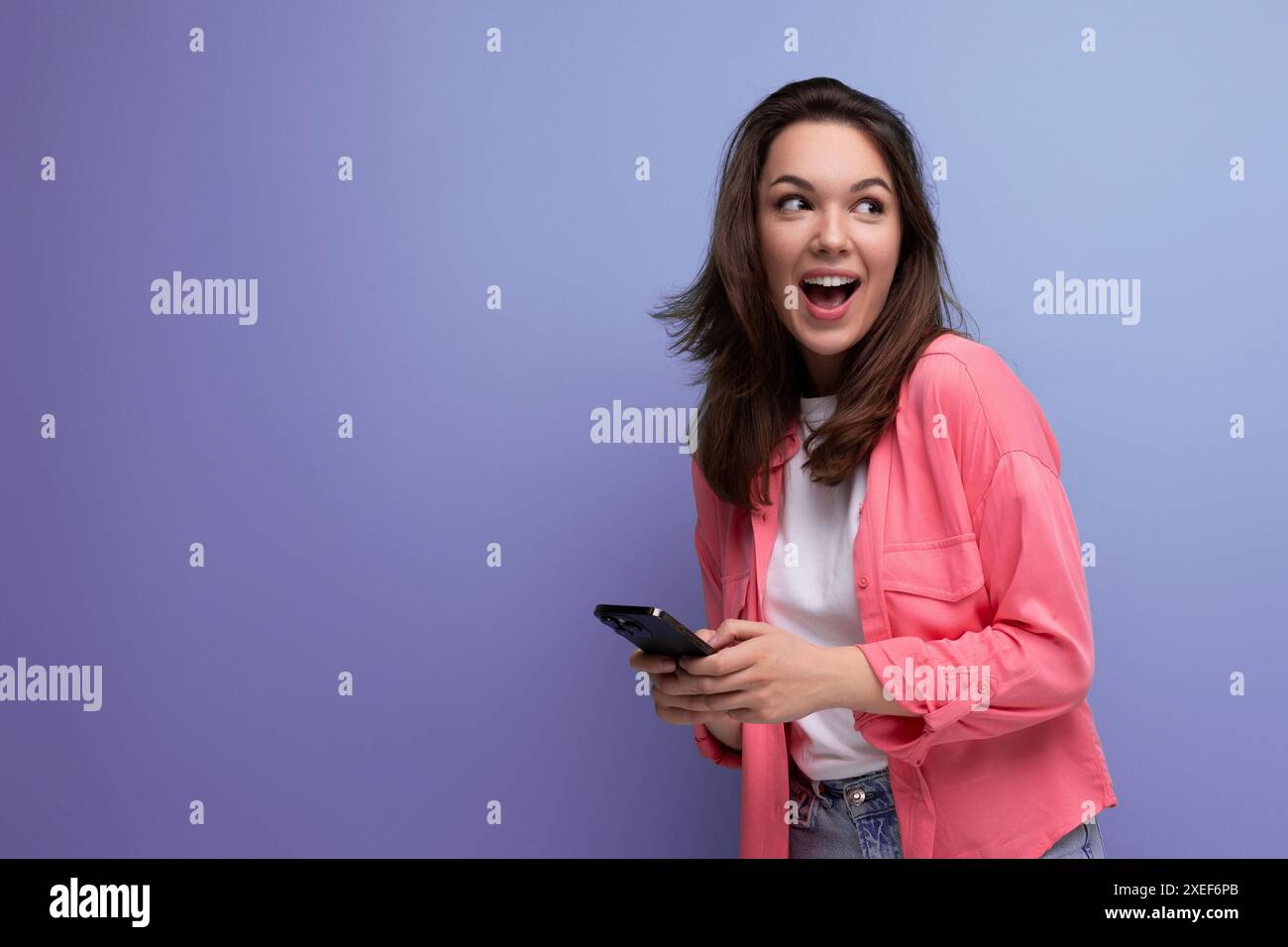 Bruna giovane donna con i capelli a spalla in una camicia rosa con uno smartphone isolato su uno sfondo semplice Foto Stock Bruna giovane donna con i capelli a spalla in una camicia rosa con uno smartphone isolato su uno sfondo semplice Foto Stock