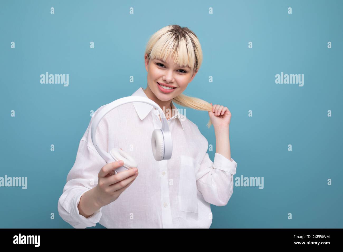 Una giovane donna bionda di successo che lavora in ufficio con camicia bianca e jeans usa le cuffie durante una pausa. concetto di business Foto Stock