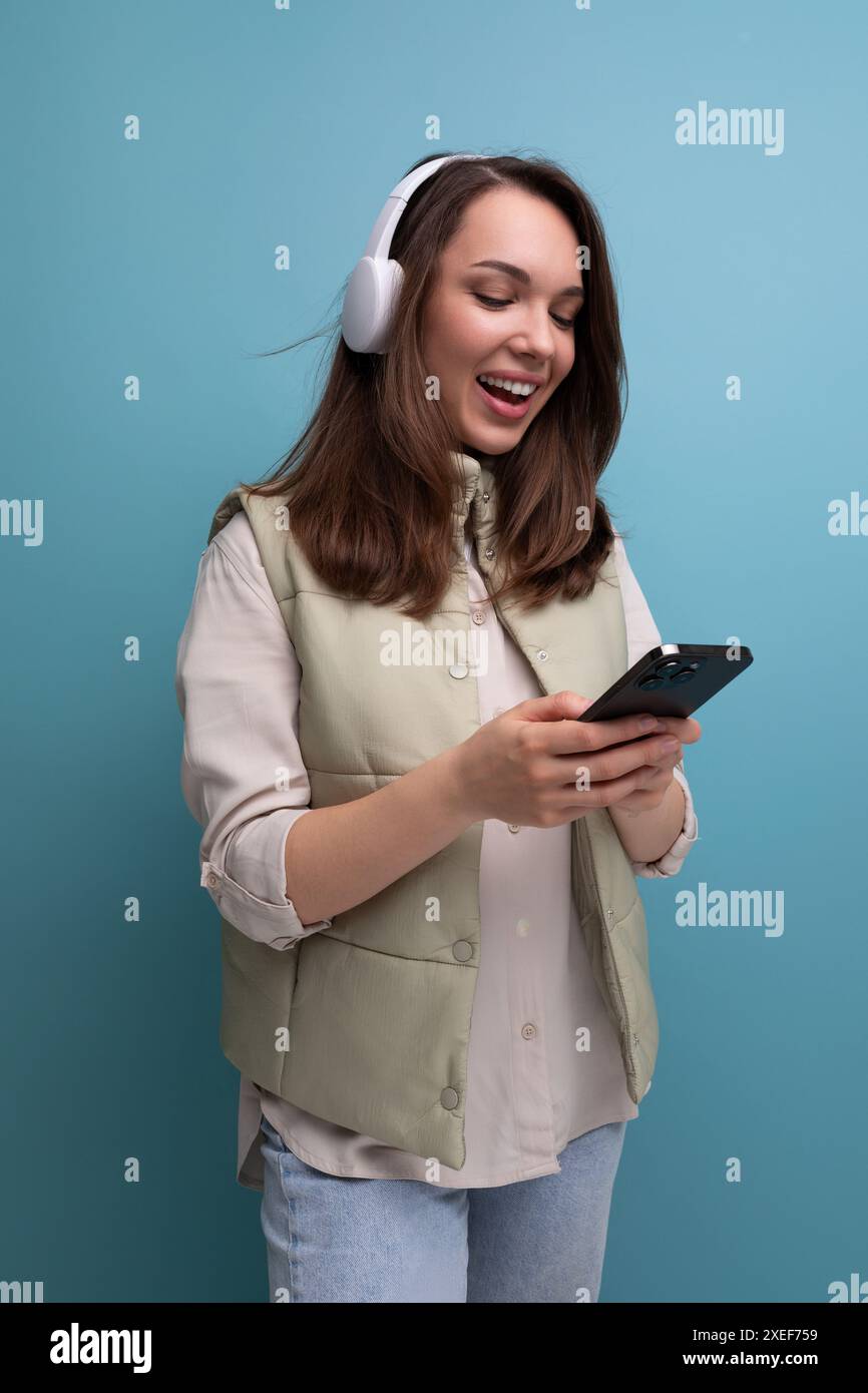 Una donna positiva degli anni '30 comunica su Internet utilizzando le cuffie e il telefono cellulare Foto Stock