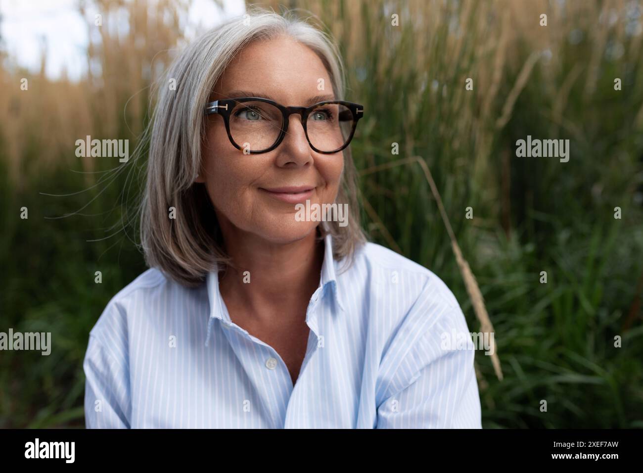 Una donna d'affari dai capelli grigi, slanciata e carina, donna caucasica di anni maturi con una camicia leggera, cammina per strada Foto Stock