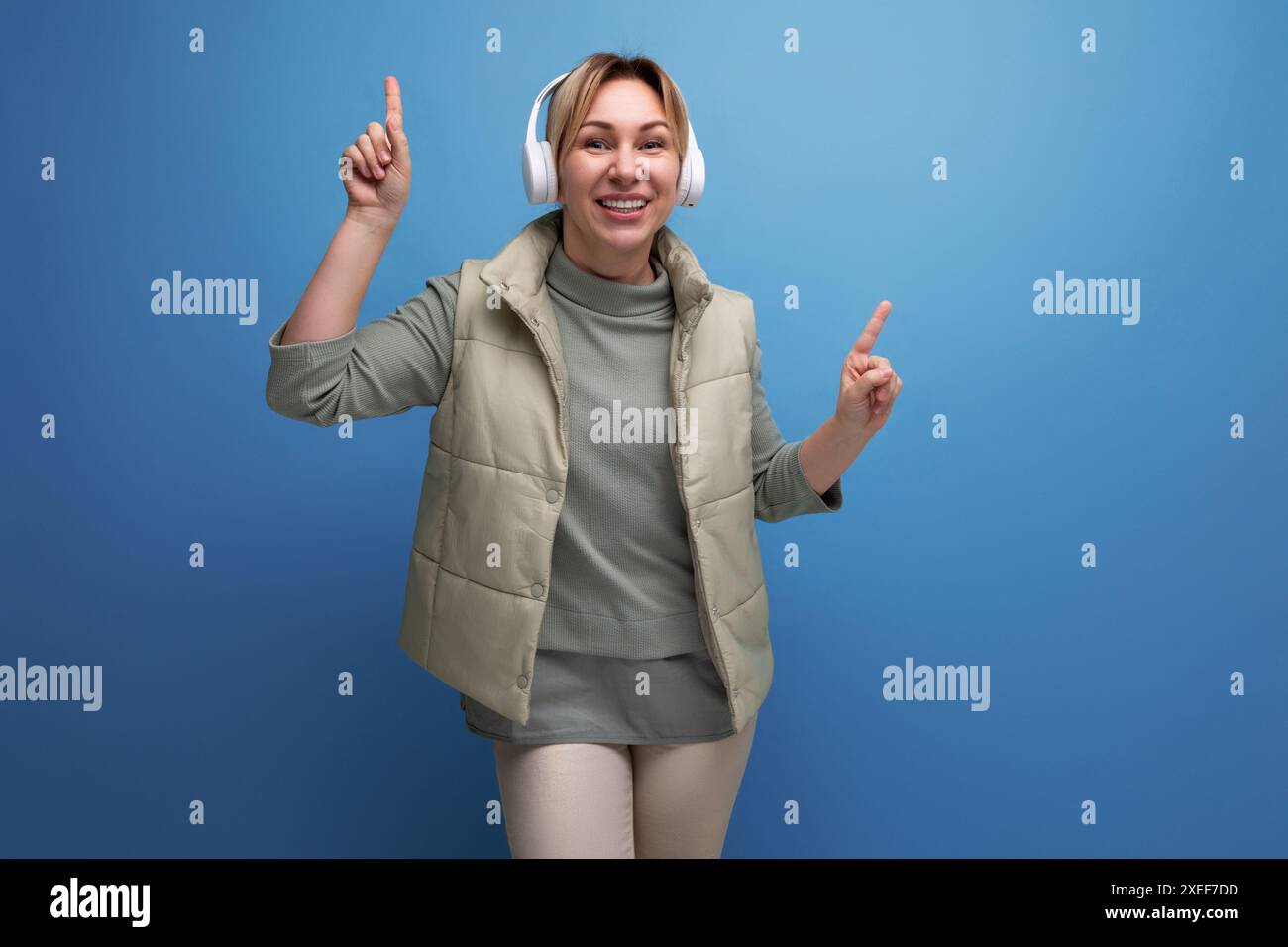 Donna millenaria bionda che ascolta musica con cuffie bianche sullo sfondo dello studio Foto Stock