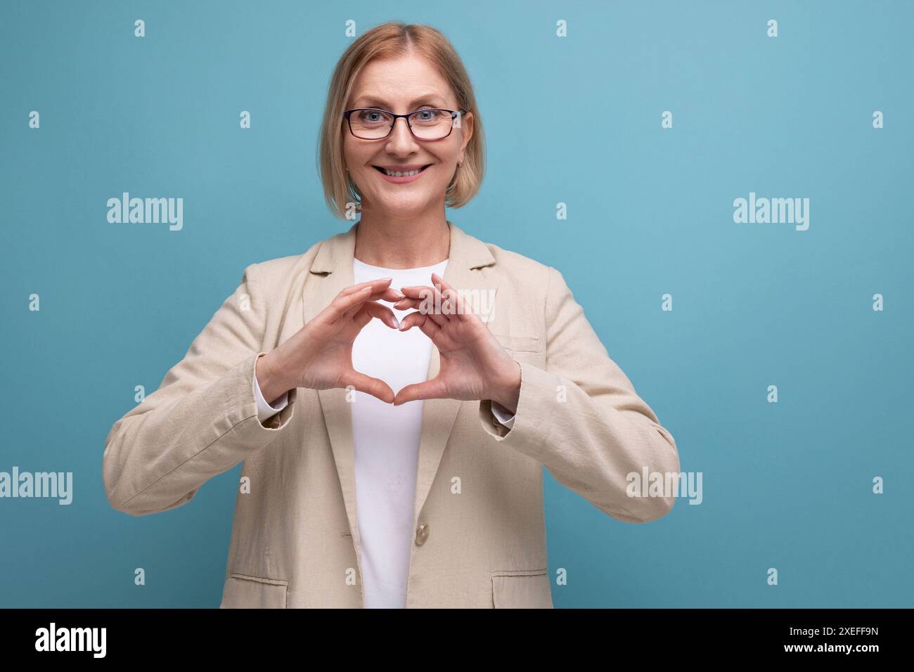 Allegra donna matura in un'immagine elegante mostra un cuore con le mani su uno sfondo luminoso dello studio con spazio di copia Foto Stock
