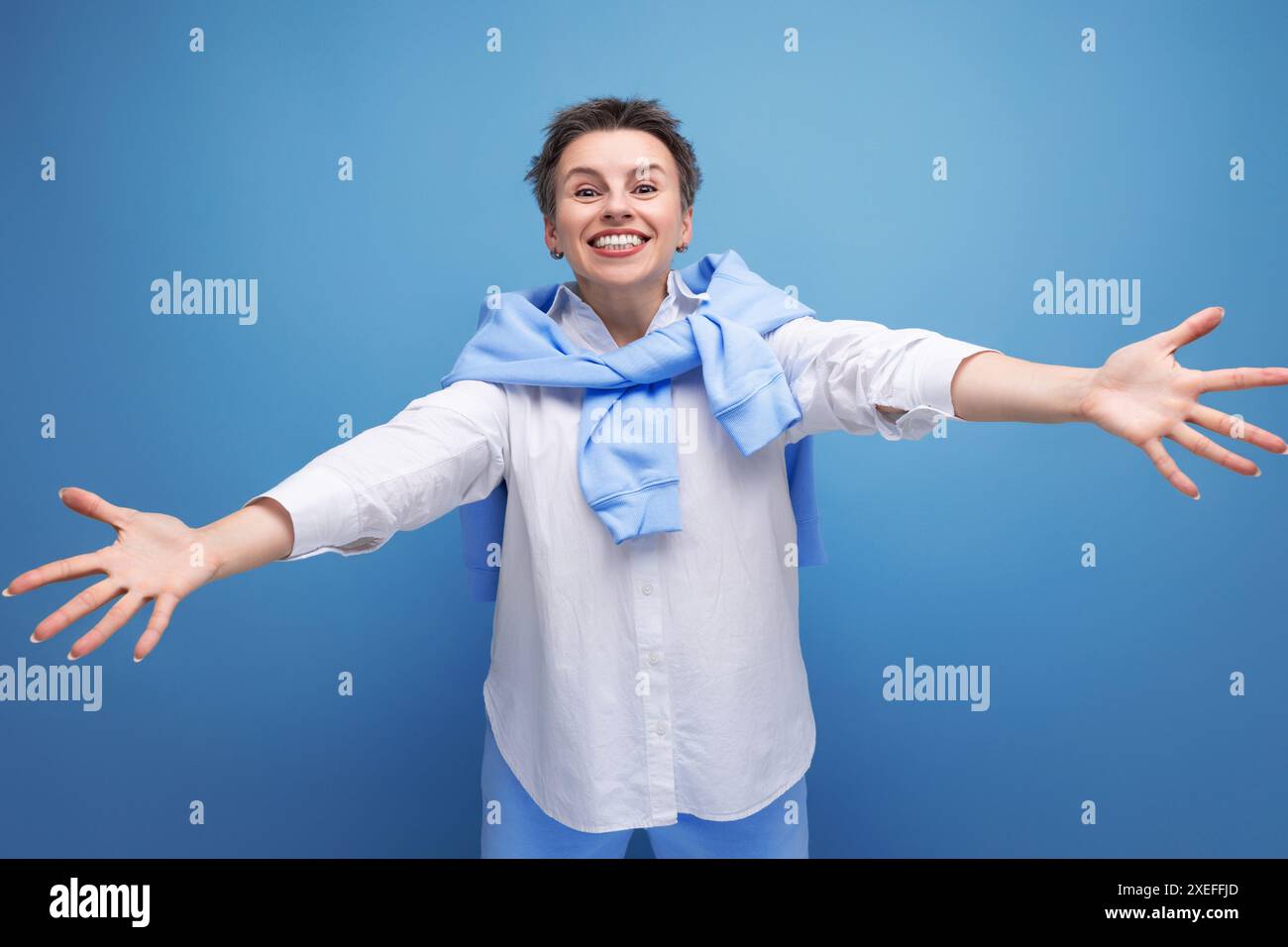 La giovane donna dai capelli scuri con i capelli aderenti in una camicia bianca si allunga le braccia per un abbraccio Foto Stock
