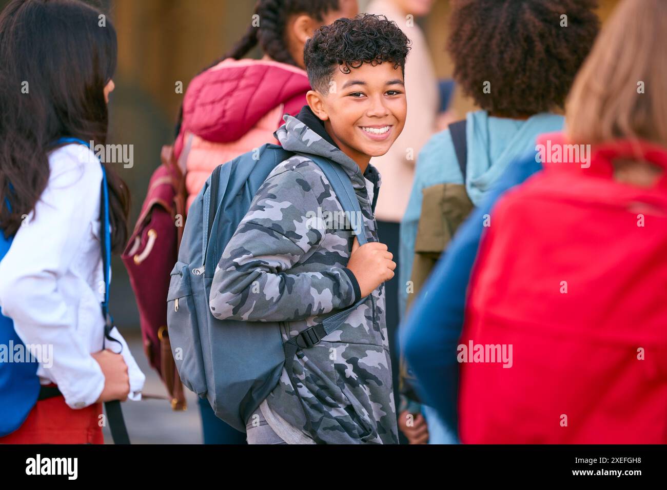 Ritratto dello studente di scuola secondaria o superiore maschile fuori dall'edificio scolastico con insegnanti e alunni Foto Stock