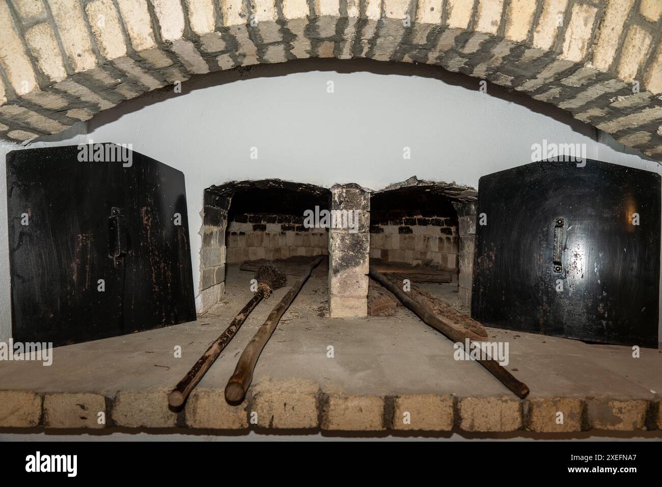 Due tradizionali forni in mattoni a legna con porte di ferro aperte e utensili con manico lungo appoggiati sul focolare dei mattoni Foto Stock