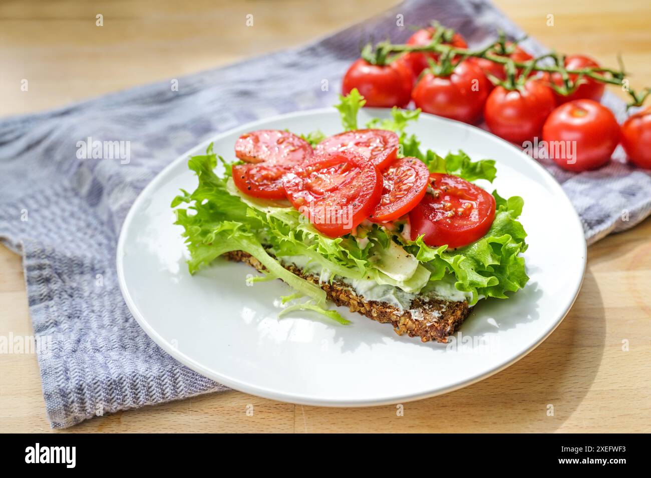 Pomodoro e lattuga su una fetta di pane integrale, panino sano su un piatto bianco, asciugamano da cucina blu e un tavolo di legno, spazio copia, focu selezionata Foto Stock