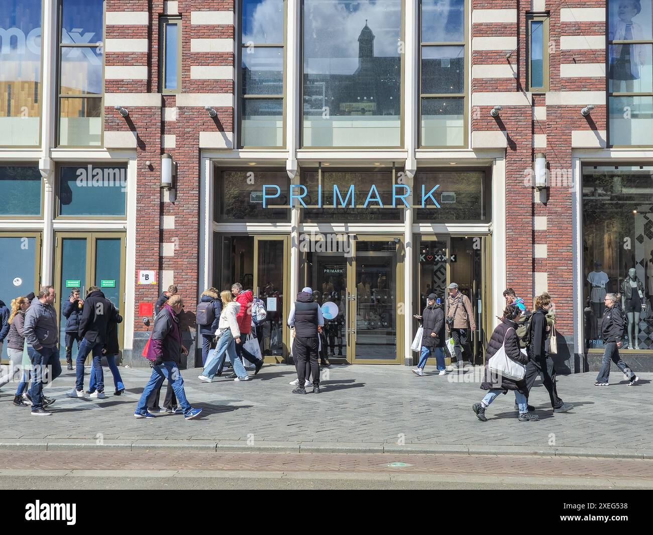 Un gruppo eterogeneo di individui passeggia tranquillamente davanti a un negozio Primark, ognuno perso nei propri pensieri, assorbendo la grandezza e la bellezza Foto Stock