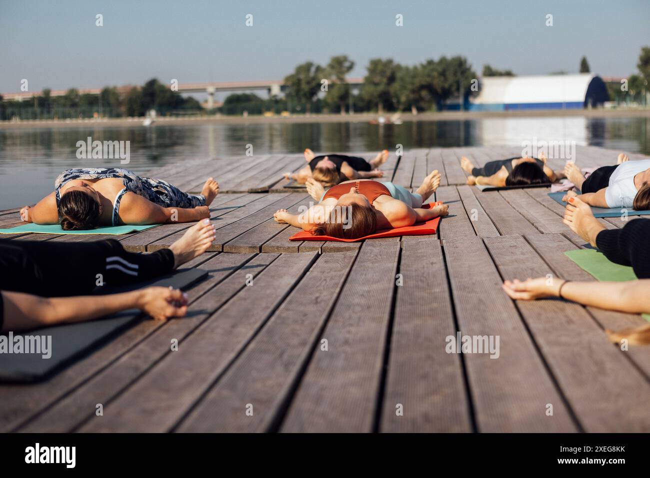 Lezione di yoga mattutina con istruttore presso il porticciolo della città. Giovani donne sane giacciono in shawasan su tappeti vicino al fiume. Foto Stock