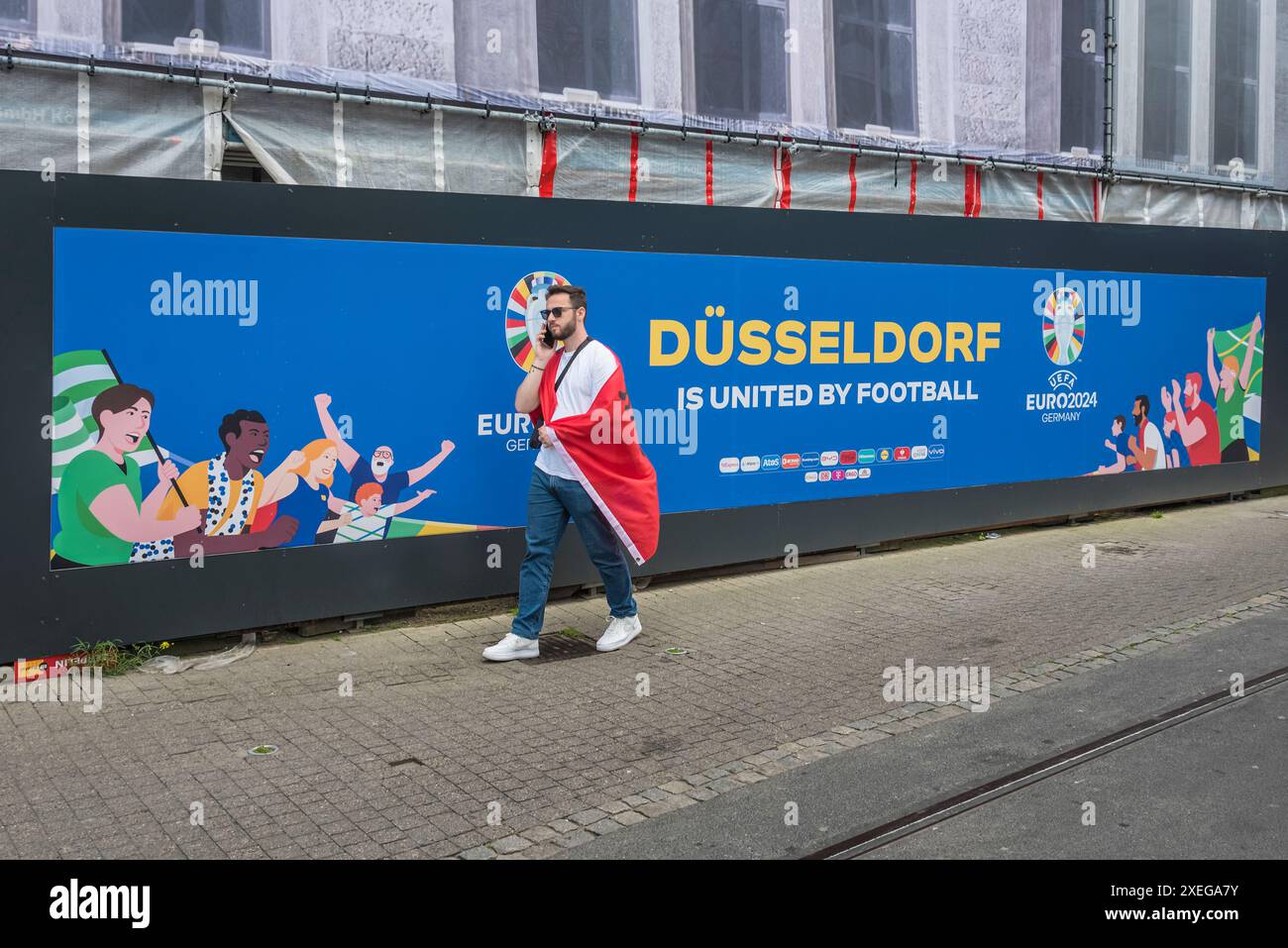 Un tifoso albanese passa un enorme cartello UEFA nella città vecchia di Düsseldorf durante la competizione calcistica internazionale EURO 2024 Foto Stock
