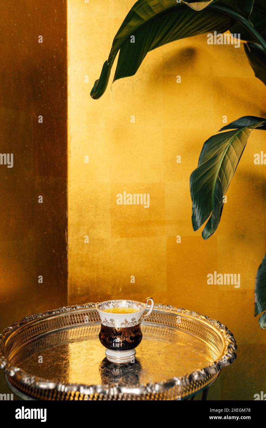 tè vintage bianco nero con motivo floreale oro e tè allo zafferano giallo su vassoio argento con sfondo dorato Foto Stock