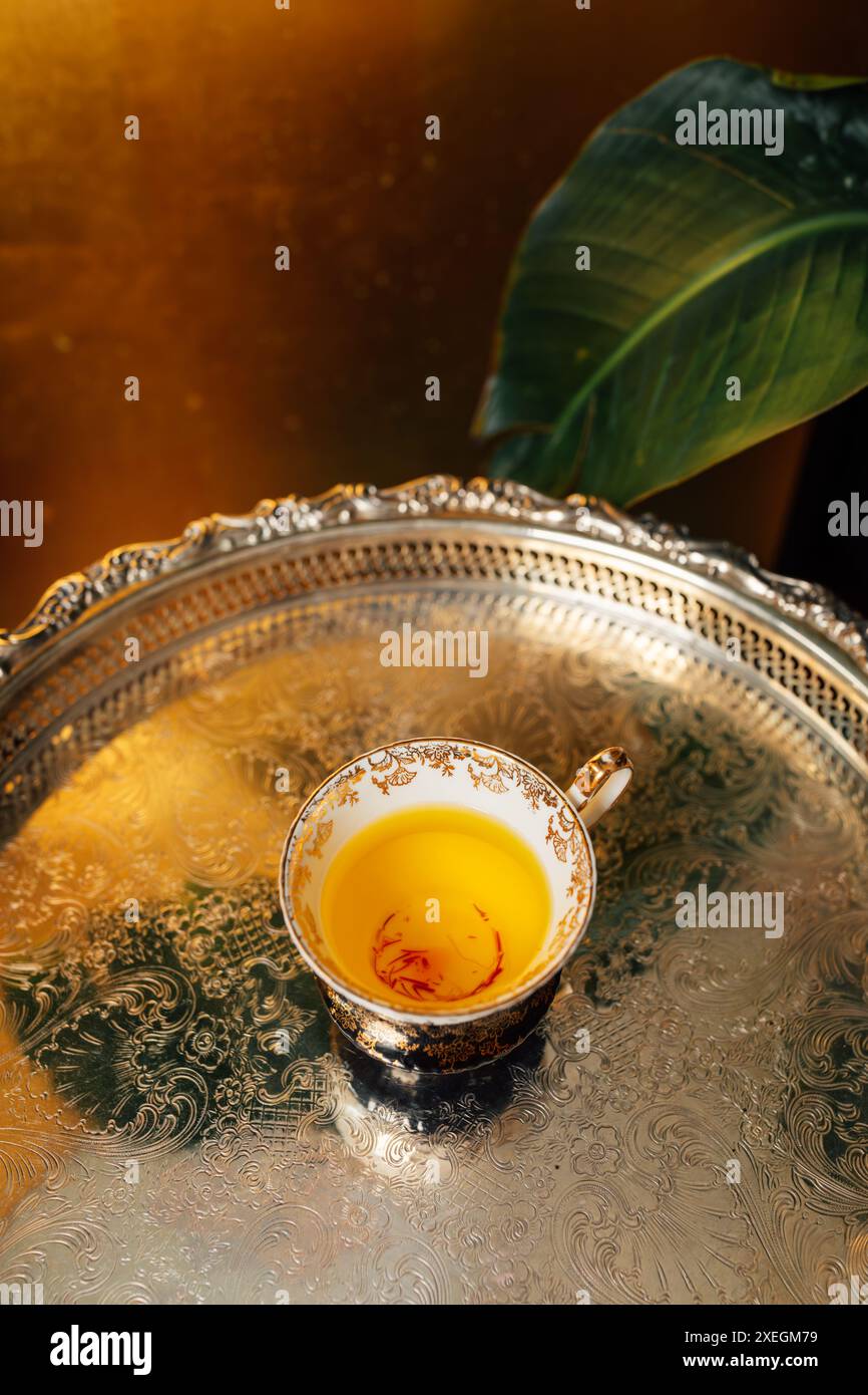 tè vintage bianco nero con motivo floreale oro e tè allo zafferano giallo su vassoio argento con sfondo dorato Foto Stock