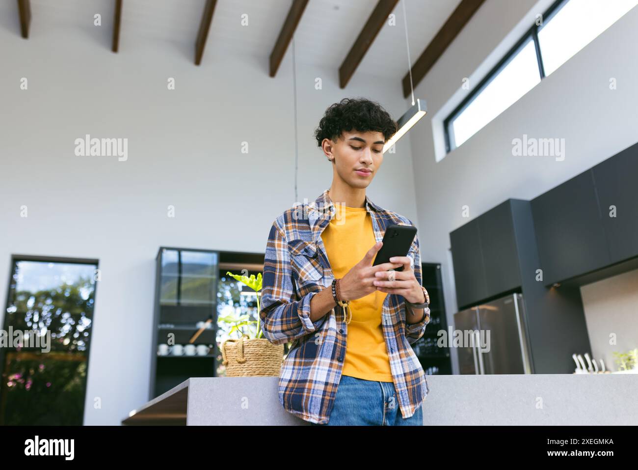 Utilizzando smartphone, adolescente in piedi in cucina moderna, a controllare i messaggi Foto Stock