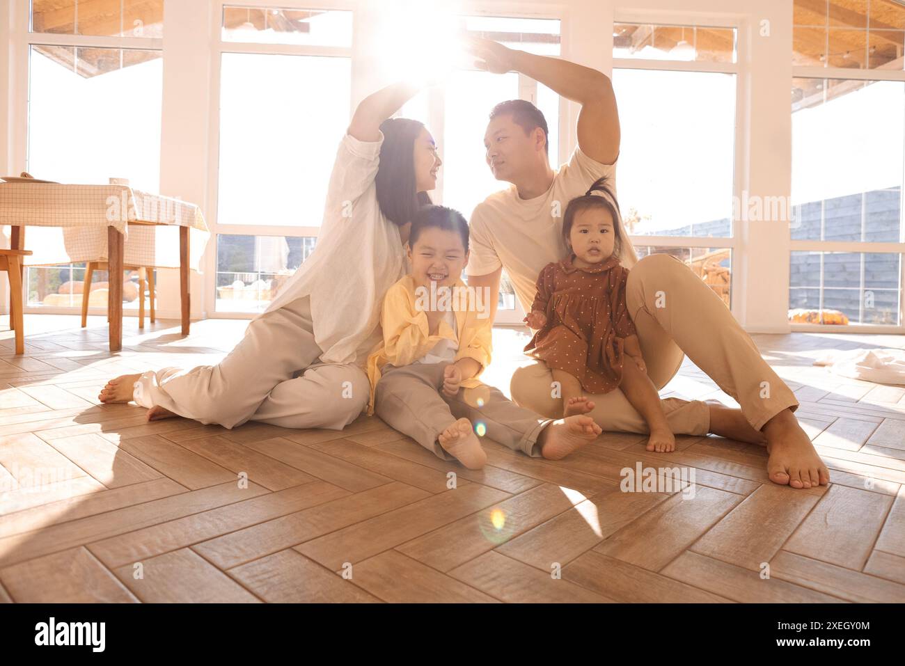 Genitori asiatici che creano un tetto simbolico di mani sopra i loro carini figli. La famiglia felice con i bambini piccoli si diverte a trasferirsi a New, o Foto Stock