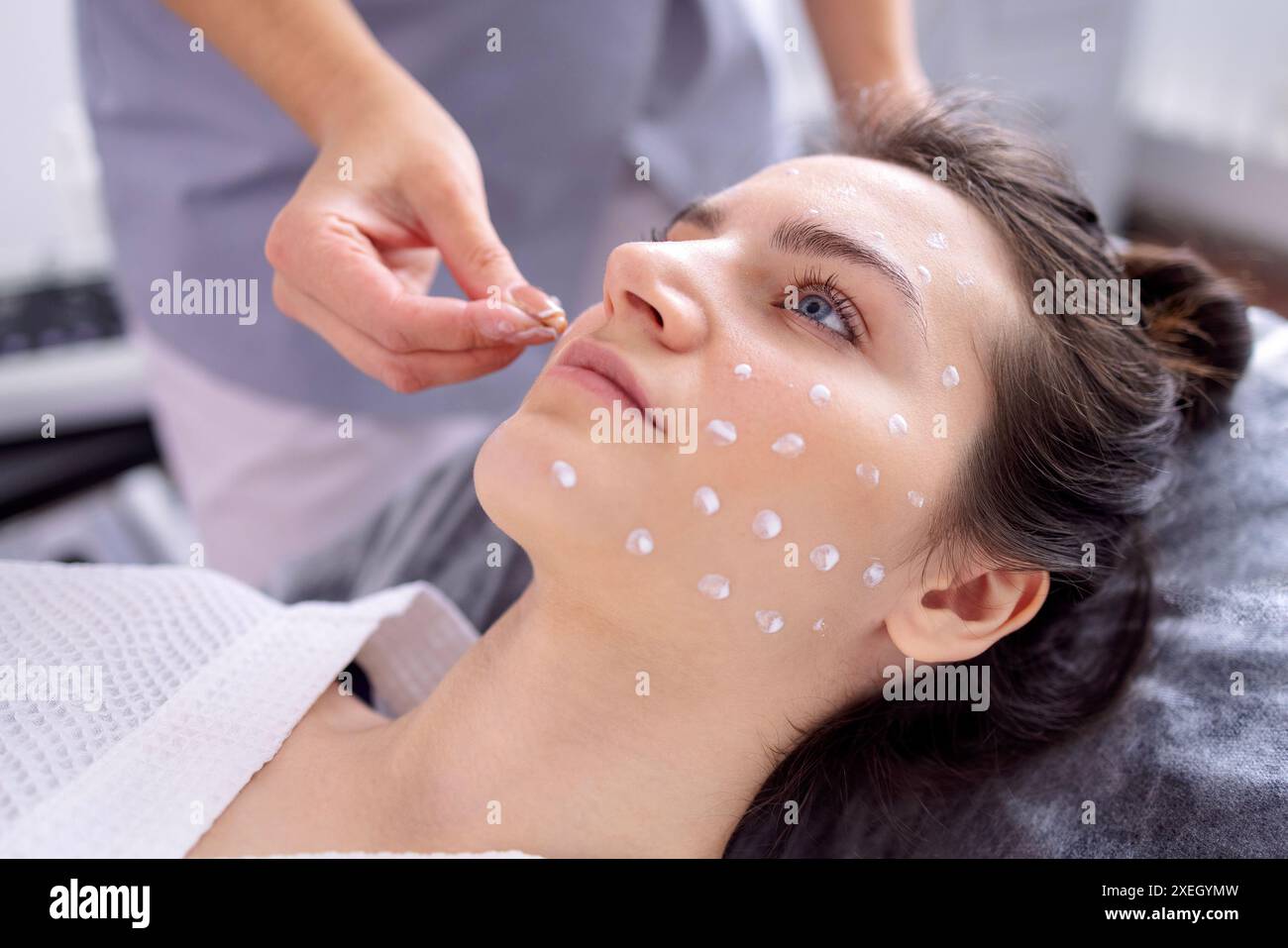 Il primo piano dell'estetista applica la crema di ampolla al viso di una cliente femminile nel salone spa Foto Stock