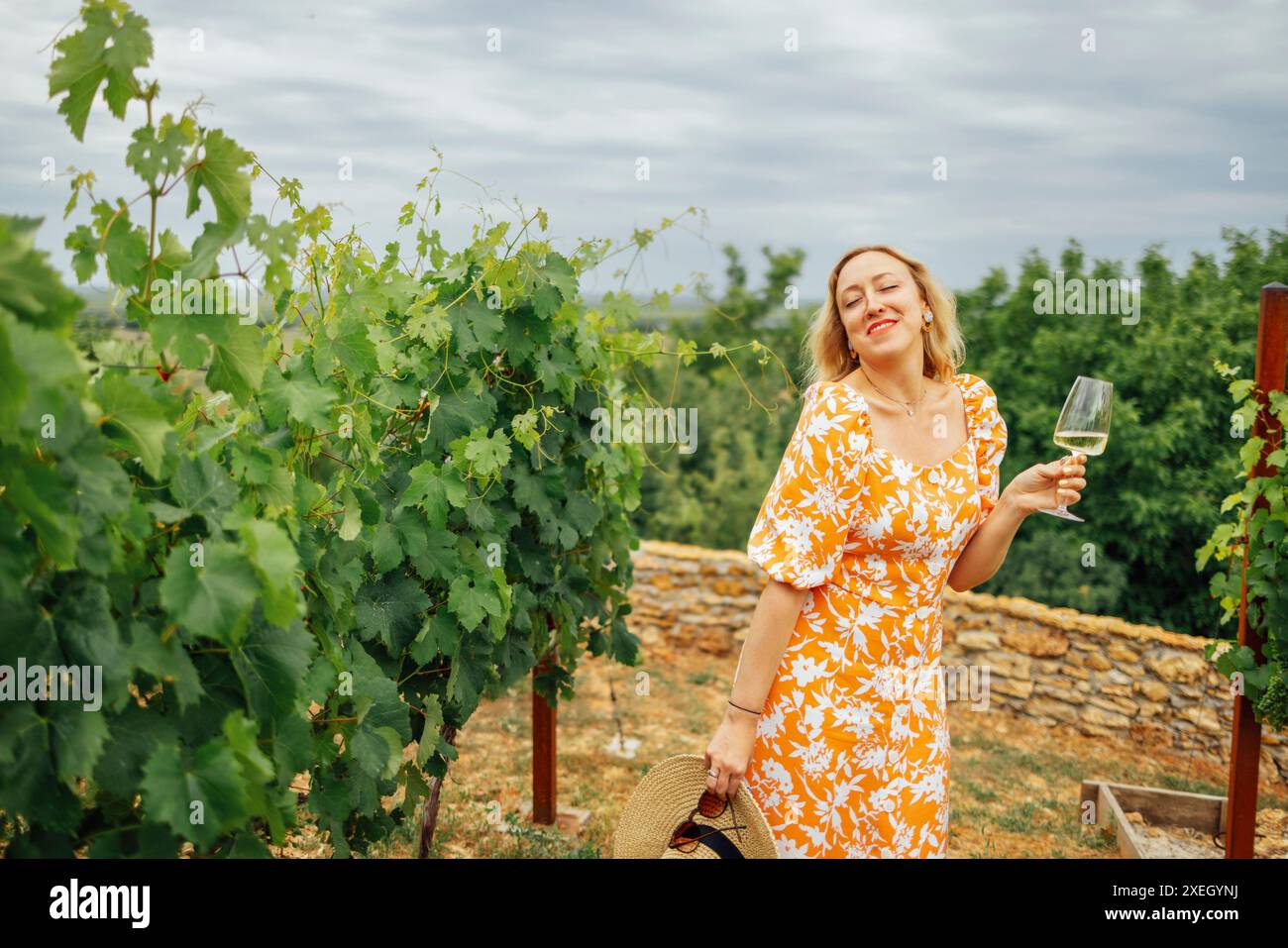Allegra donna bionda in abito arancione brillante con stampa floreale, regge un bicchiere di champagne Foto Stock