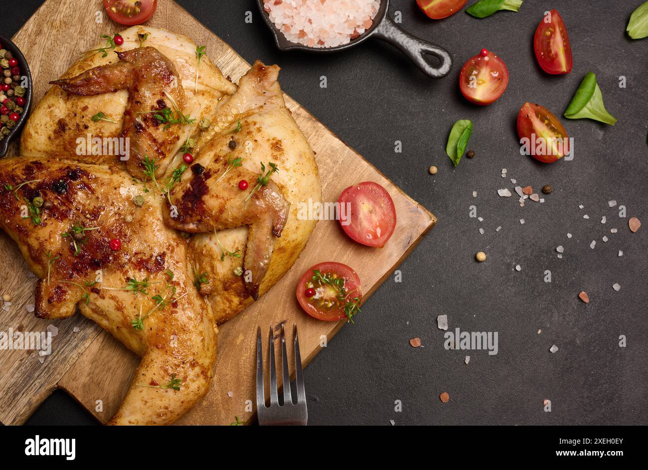 Pollo intero fritto con spezie su un tavolo di legno su un tavolo nero Foto Stock