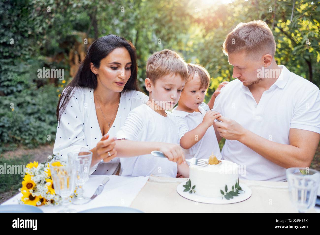 Mamma, papà e due figli in abiti bianchi mangiano la torta in un caffè all'aperto Foto Stock