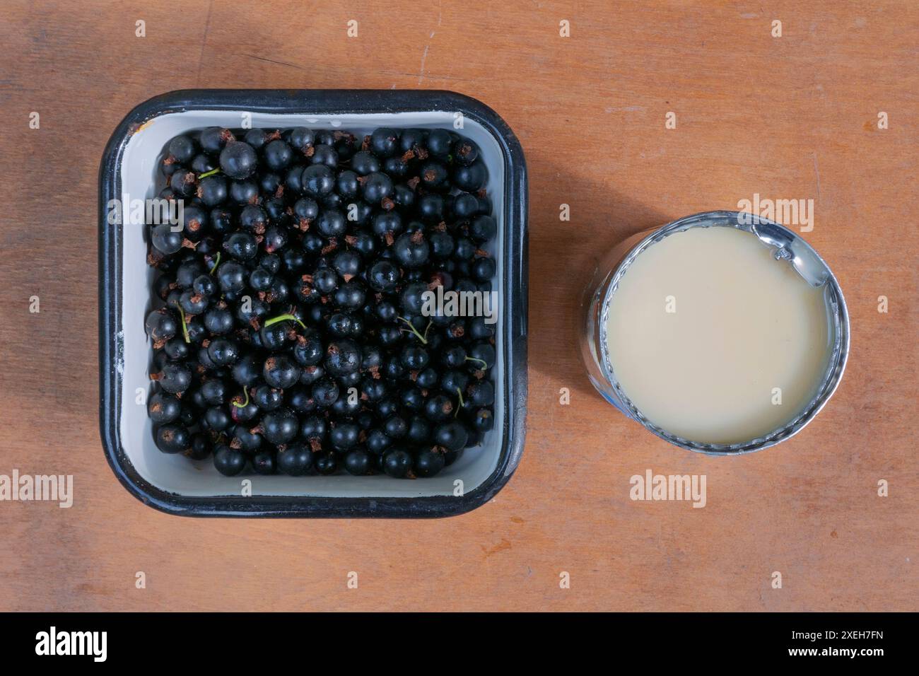 Lattina di latte condensato aperta, bacca di ribes nera in metallo su sfondo marrone in legno, vista dall'alto. Il concetto di mangiare sano. Foto Stock