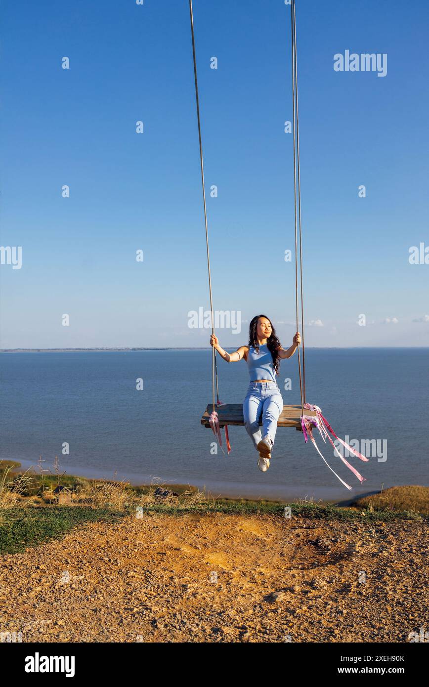 Attraente ragazza asiatica in abiti casual che oscilla su un swing all'aperto Foto Stock