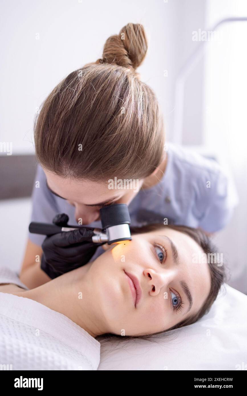 Il medico dermatologo esamina la pelle del viso del cliente del salone di bellezza con una lente dermatologica Foto Stock