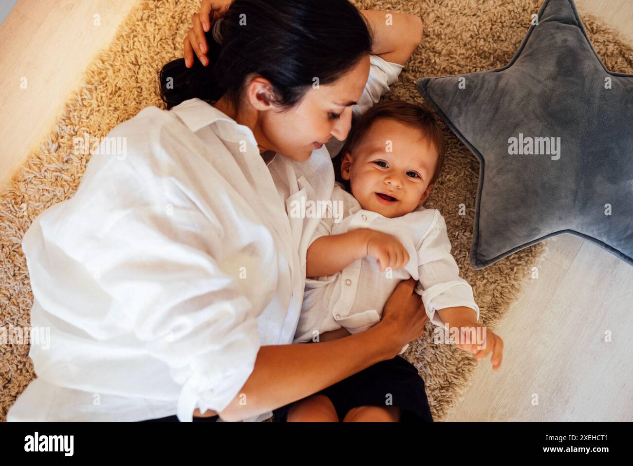 Una giovane donna sorridente e il suo bambino sono sdraiati sul pavimento della camera da letto e si divertono Foto Stock