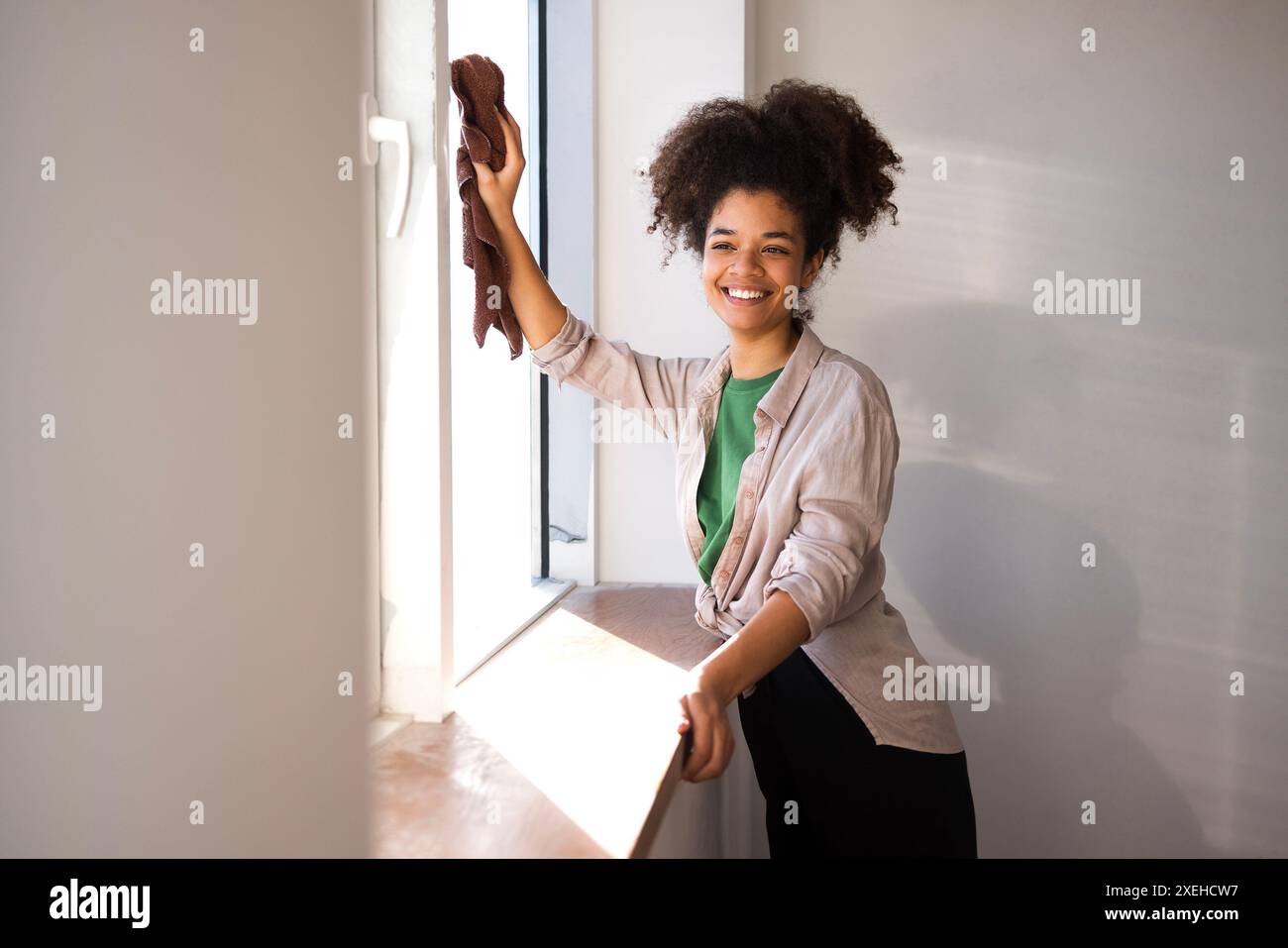 Una donna afro americana in abiti casual pulisce la finestra con uno straccio Foto Stock