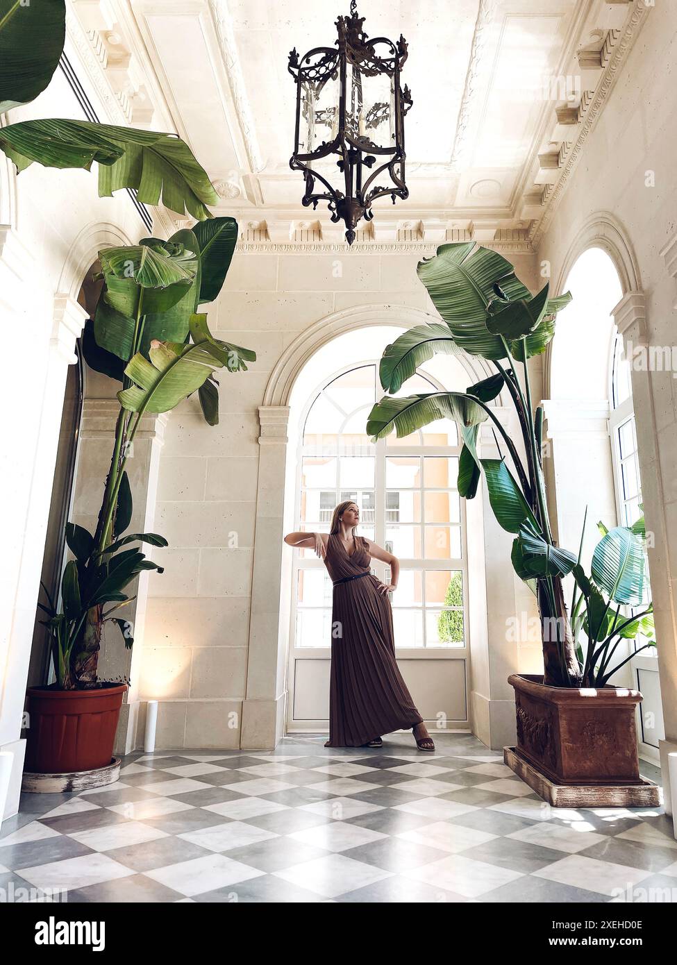 Affascinante ragazza in un elegante lungo abito fluente si erge in una posa squisita nel palazzo. Foto Stock