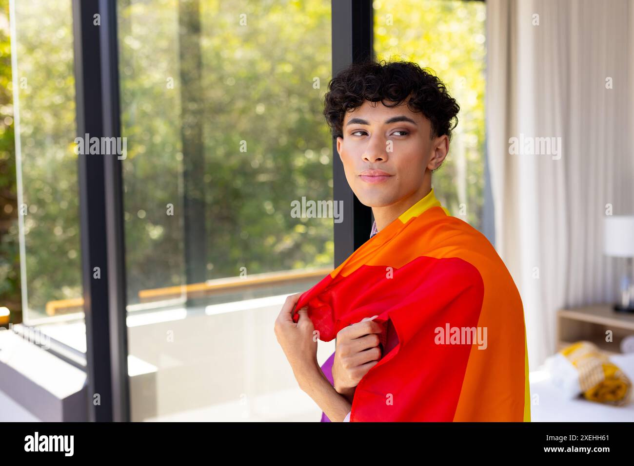 Indossando la bandiera Pride, donna transgender che si trova in una casa moderna con fiducia Foto Stock