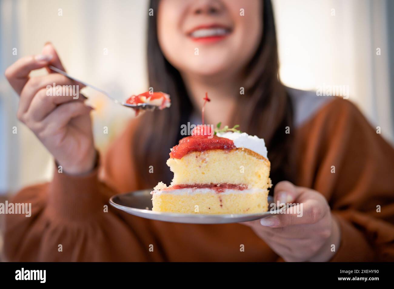 Bella donna asiatica che mangia una torta gustosa. Ragazza adolescente che mangia la torta. Foto Stock