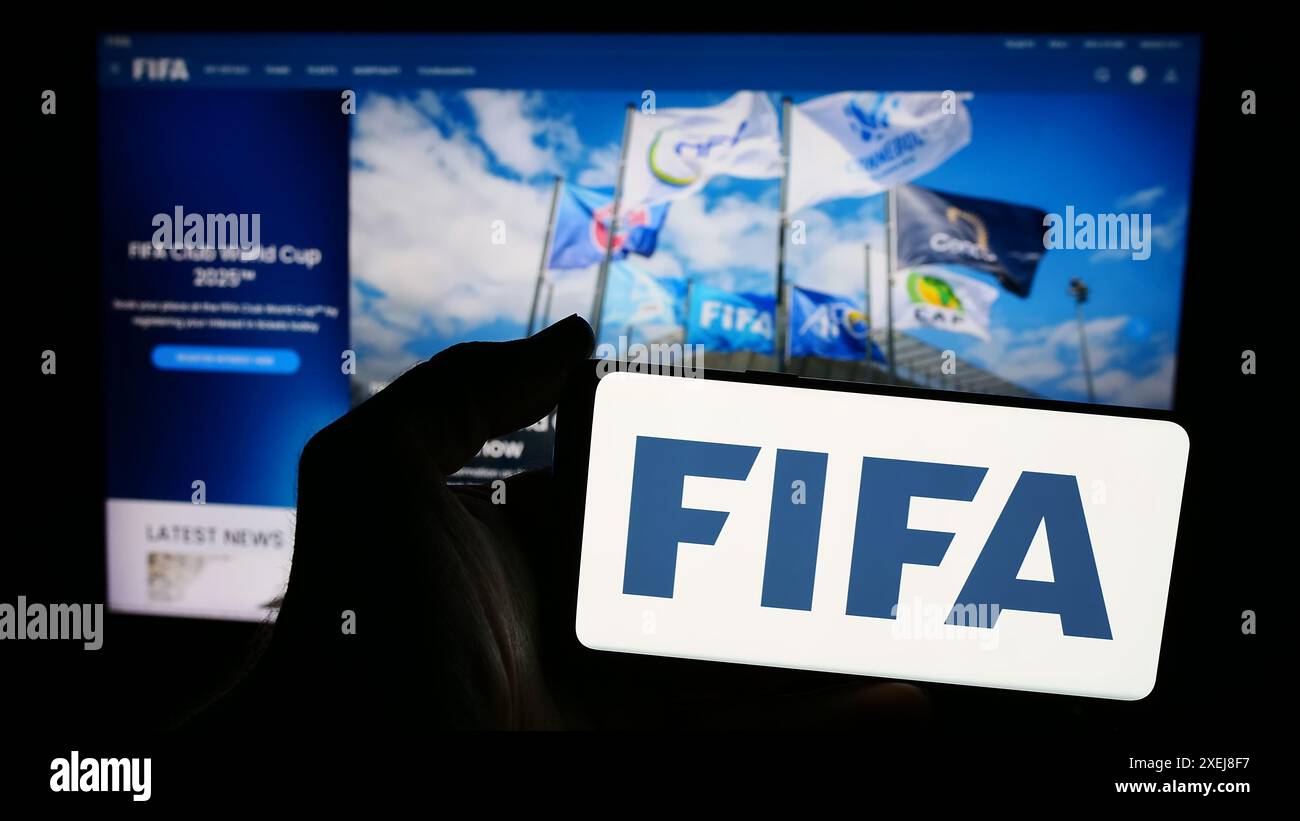 Persona con smartphone con logo della Federazione Internazionale di calcio (FIFA) davanti al sito Web. Mettere a fuoco il display del telefono. Foto Stock