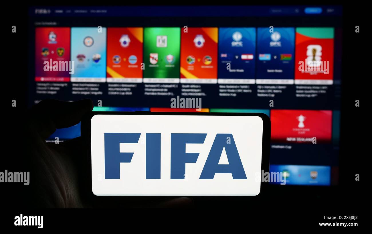 Persona che detiene un cellulare con il logo della Federazione Internazionale di calcio (FIFA) davanti alla pagina web. Mettere a fuoco il display del telefono. Foto Stock