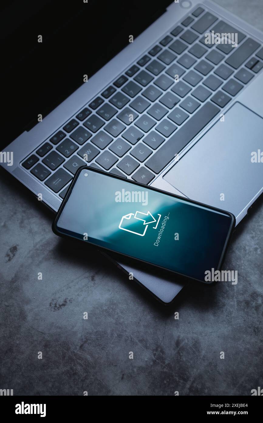 Smartphone posizionato sul laptop con interfaccia di download sullo schermo. Tecnologia di storage cloud. Aggiornamento software. Sistema di backup. Foto Stock