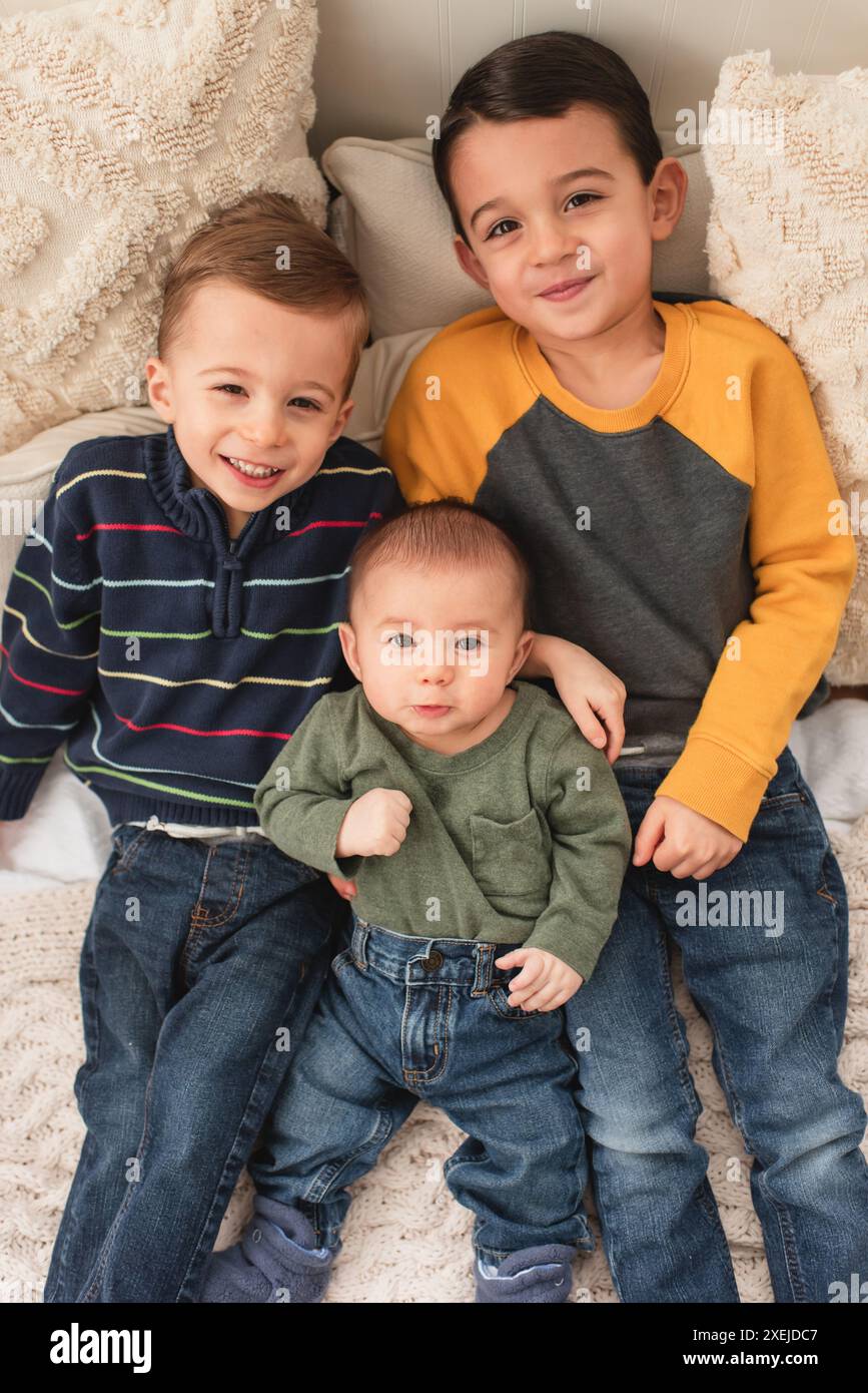 Tre fratelli sorridenti sdraiati a letto su cuscini e coperte confortevoli Foto Stock