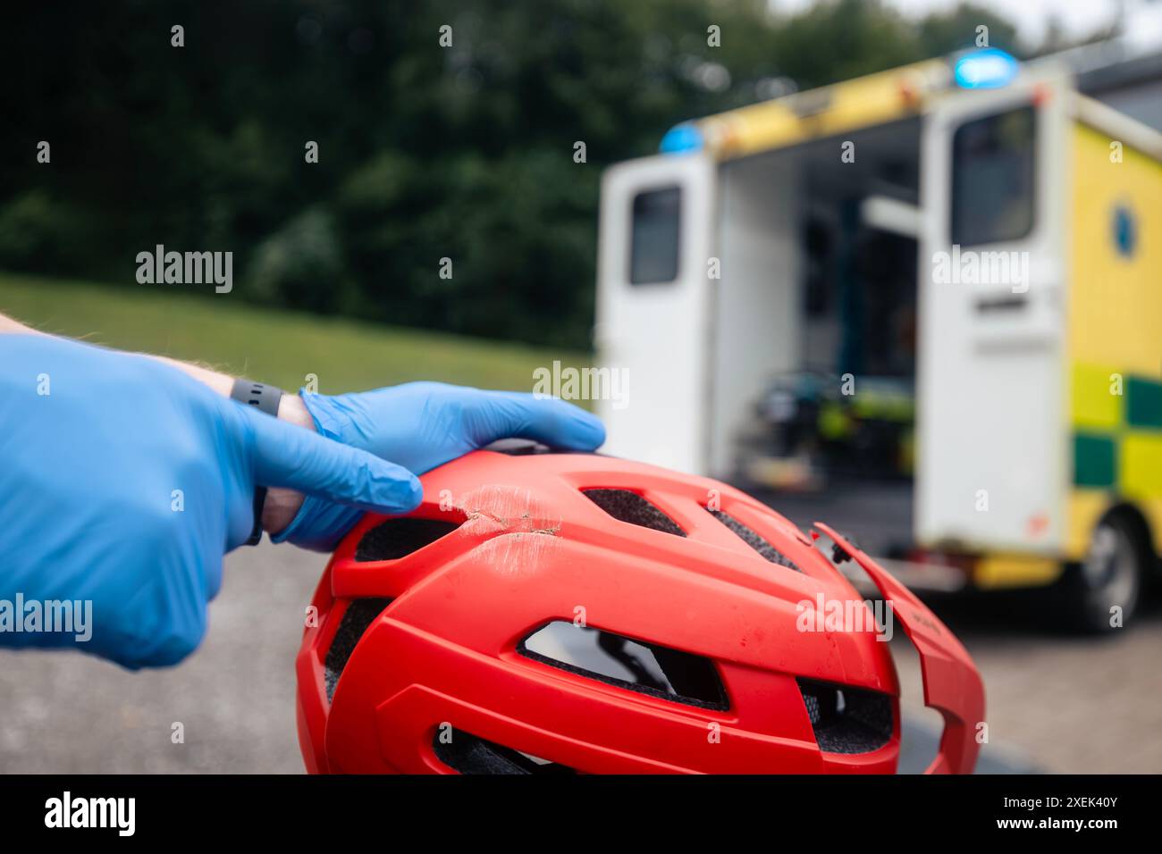 Paramedico mostrando a casco di sicurezza bicicletta rotto dopo caduta ciclista contro ambulanza auto di servizio medico di emergenza. Foto Stock