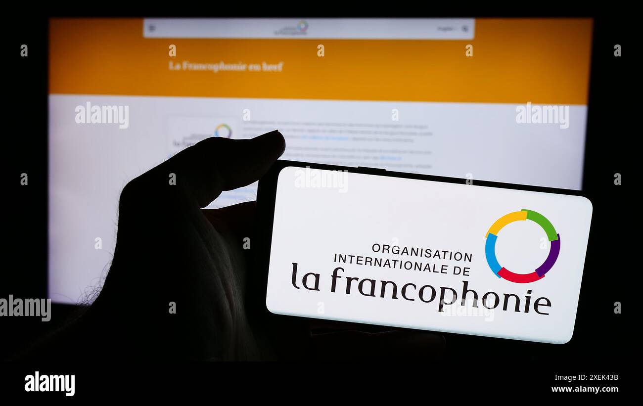 Persona che possiede un telefono cellulare con il logo dell'Organizzazione internazionale della francofonia di fronte alla pagina web. Mettere a fuoco il display del telefono. Foto Stock