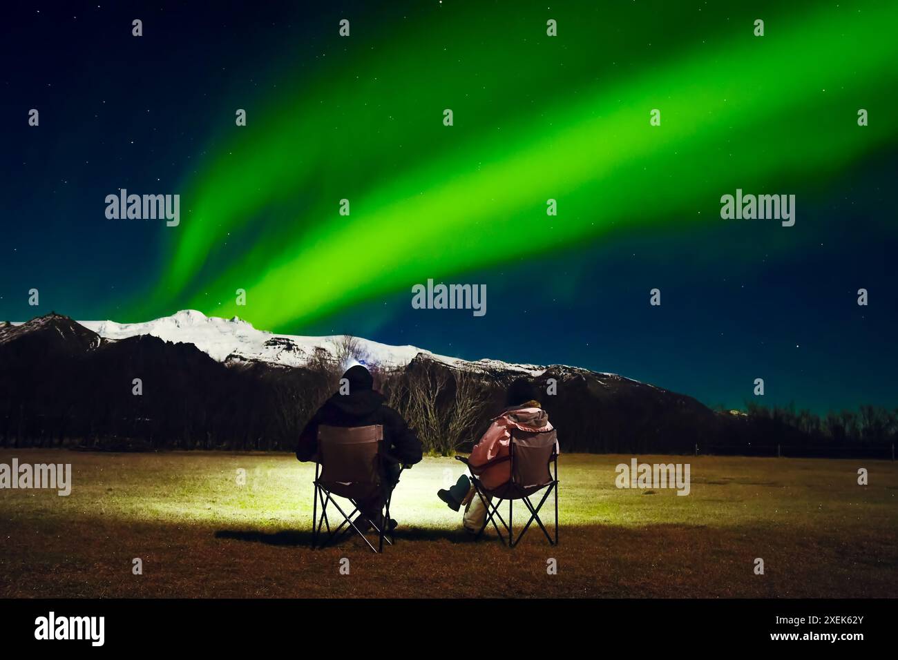 Coppia romantica in un abito nero e luminoso siediti su sedie da campeggio pieghevoli per guardare lo spettacolo dell'aurora boreale nel campeggio ufficiale. Donna e uomo all'inverno Foto Stock