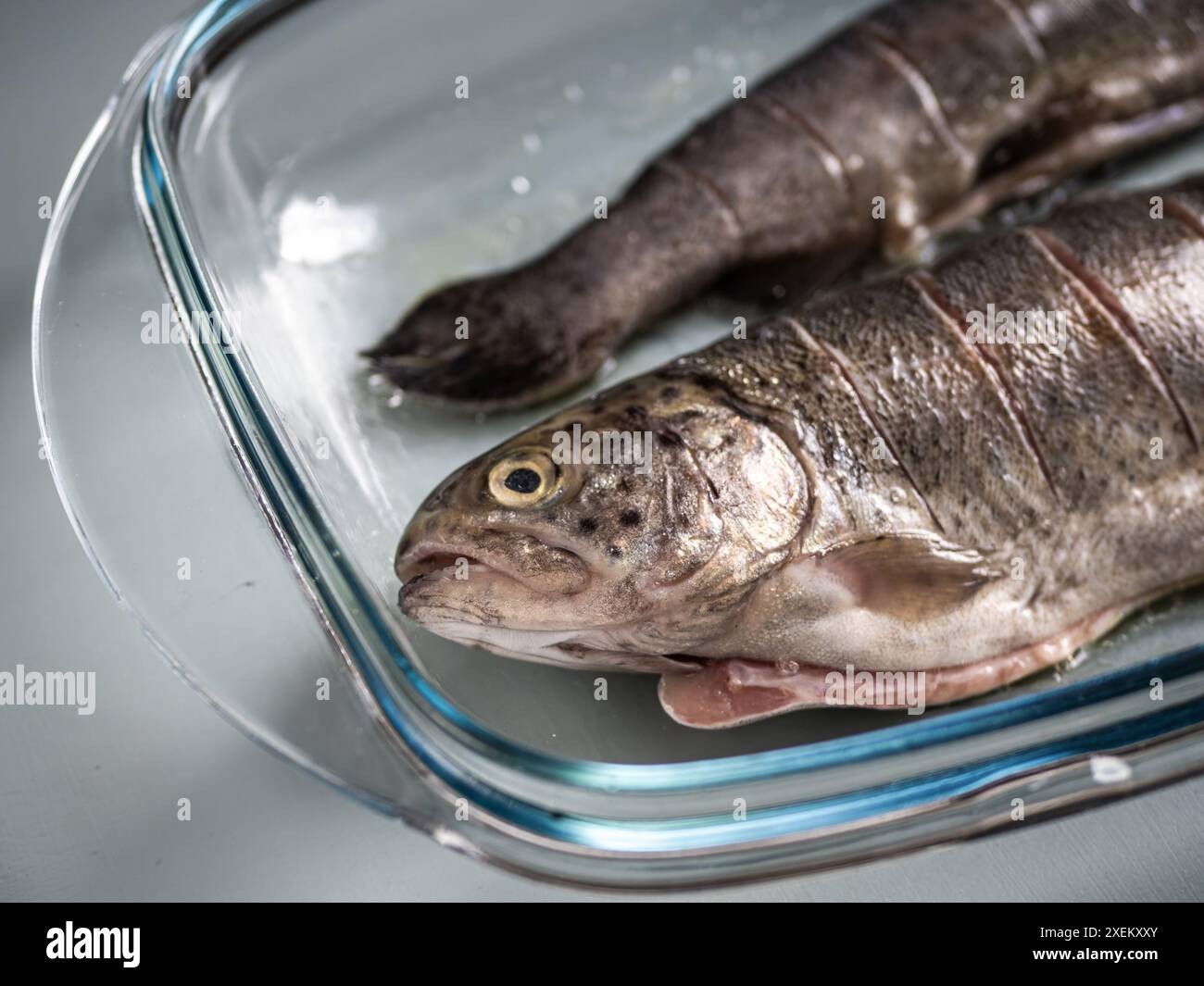 Due salmoni interi freschi con tagli laterali in una teglia da forno in vetro, preparazione del cibo, pesce arrosto, cibo per la prestata Foto Stock