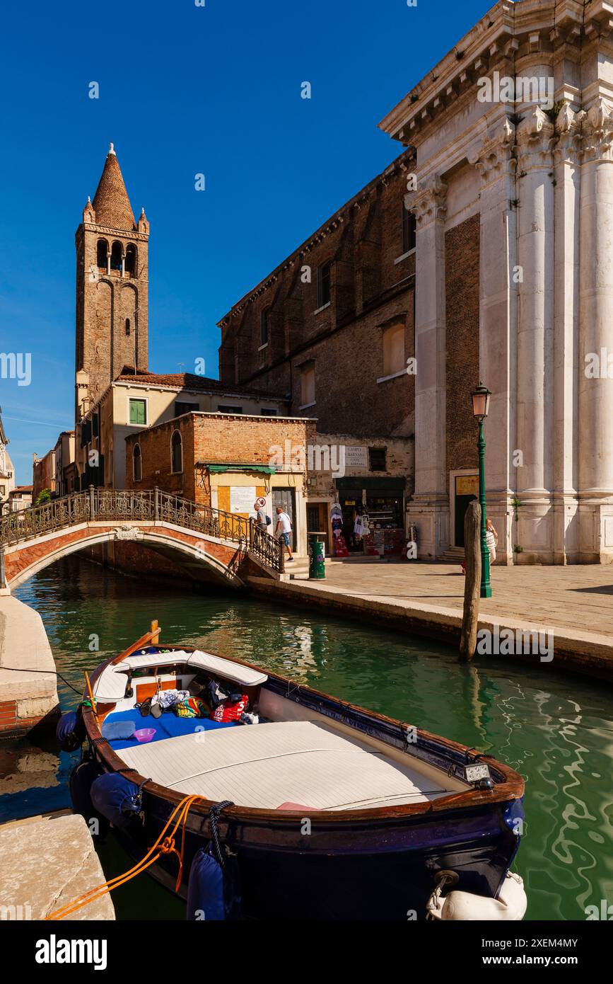 Barca che galleggia in un canale con una passerella pedonale e una torre lungo il corso d'acqua di Venezia; Venezia, Veneto, Italia Foto Stock