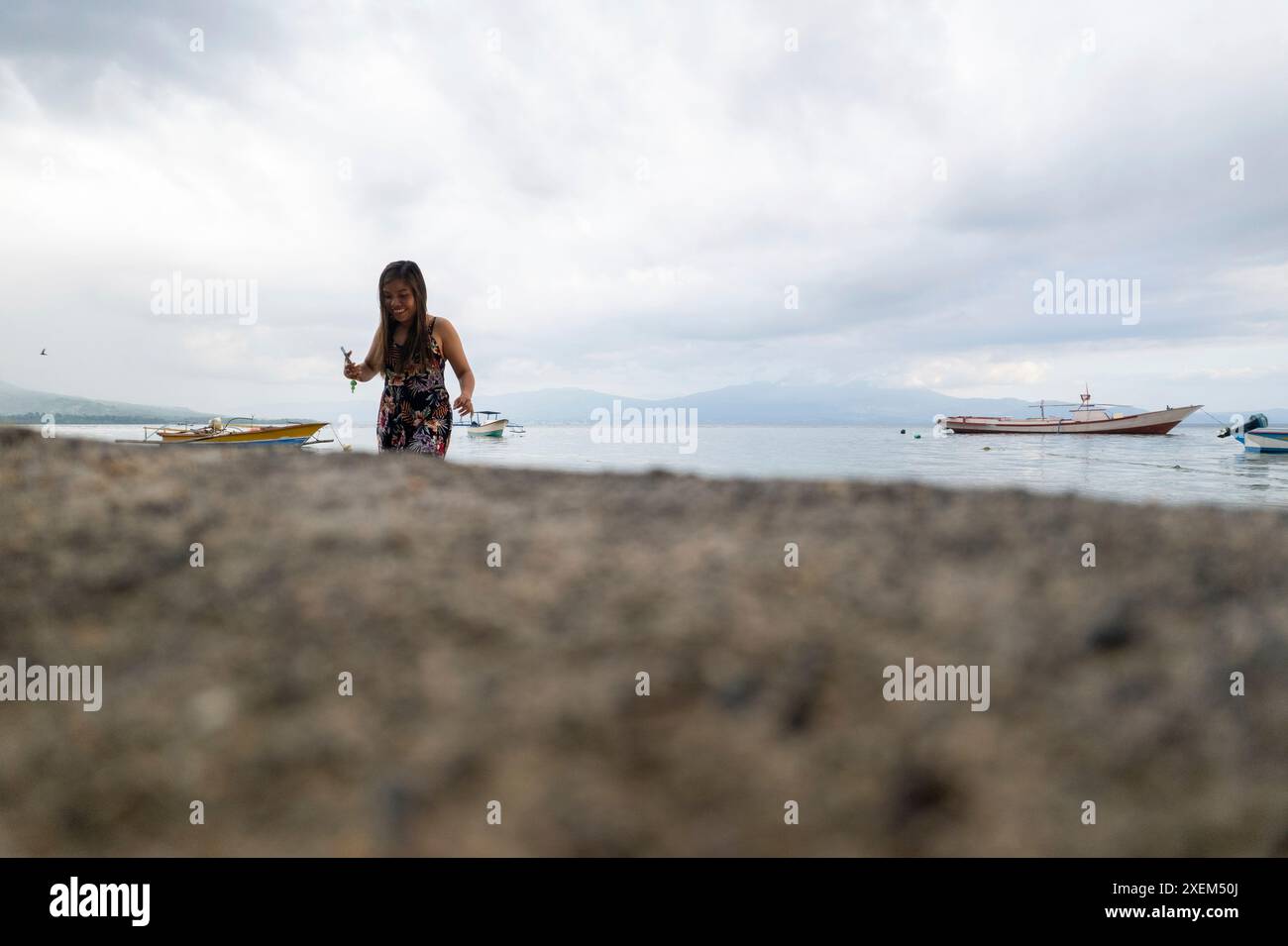 La donna ama trascorrere del tempo libero sulla spiaggia dell'isola di Bunaken, con le barche ormeggiate in acqua appena al largo della costa, North Sulawesi, Indonesia Foto Stock